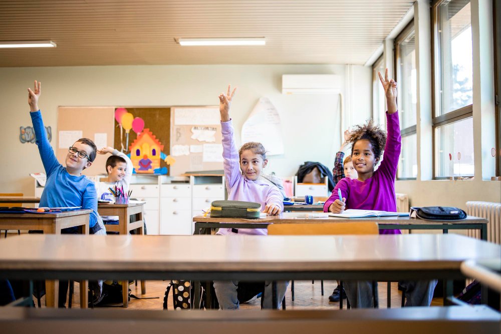 schoolchildren classroom with raised hands answering teacher s question